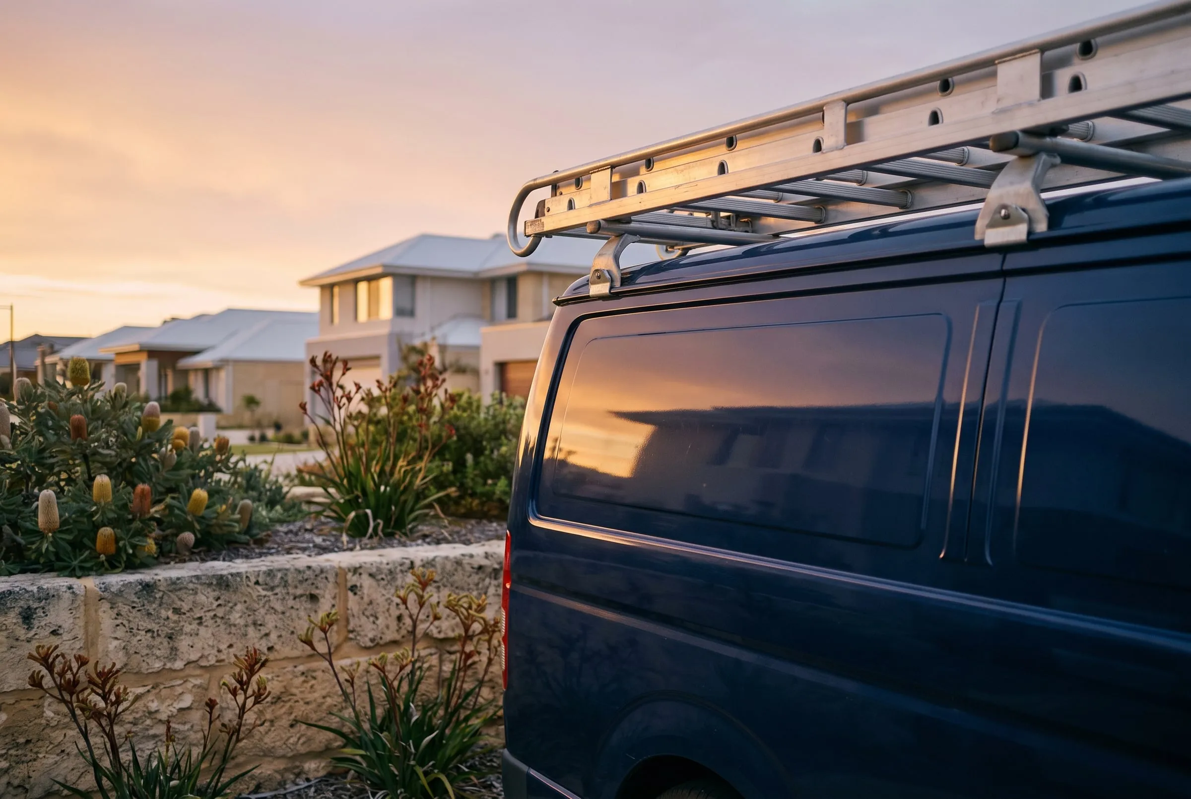 A navy work van parked on a quiet coastal street at sunset