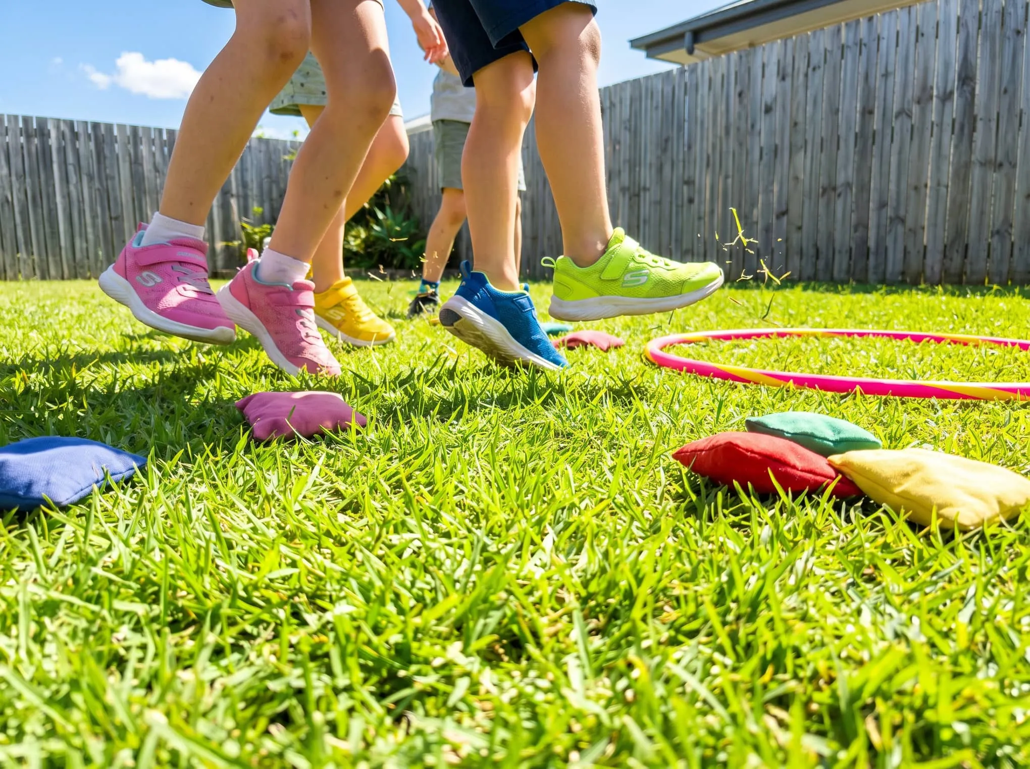 Kids' sneakers mid-race on a green lawn with bean bags and a hula hoop