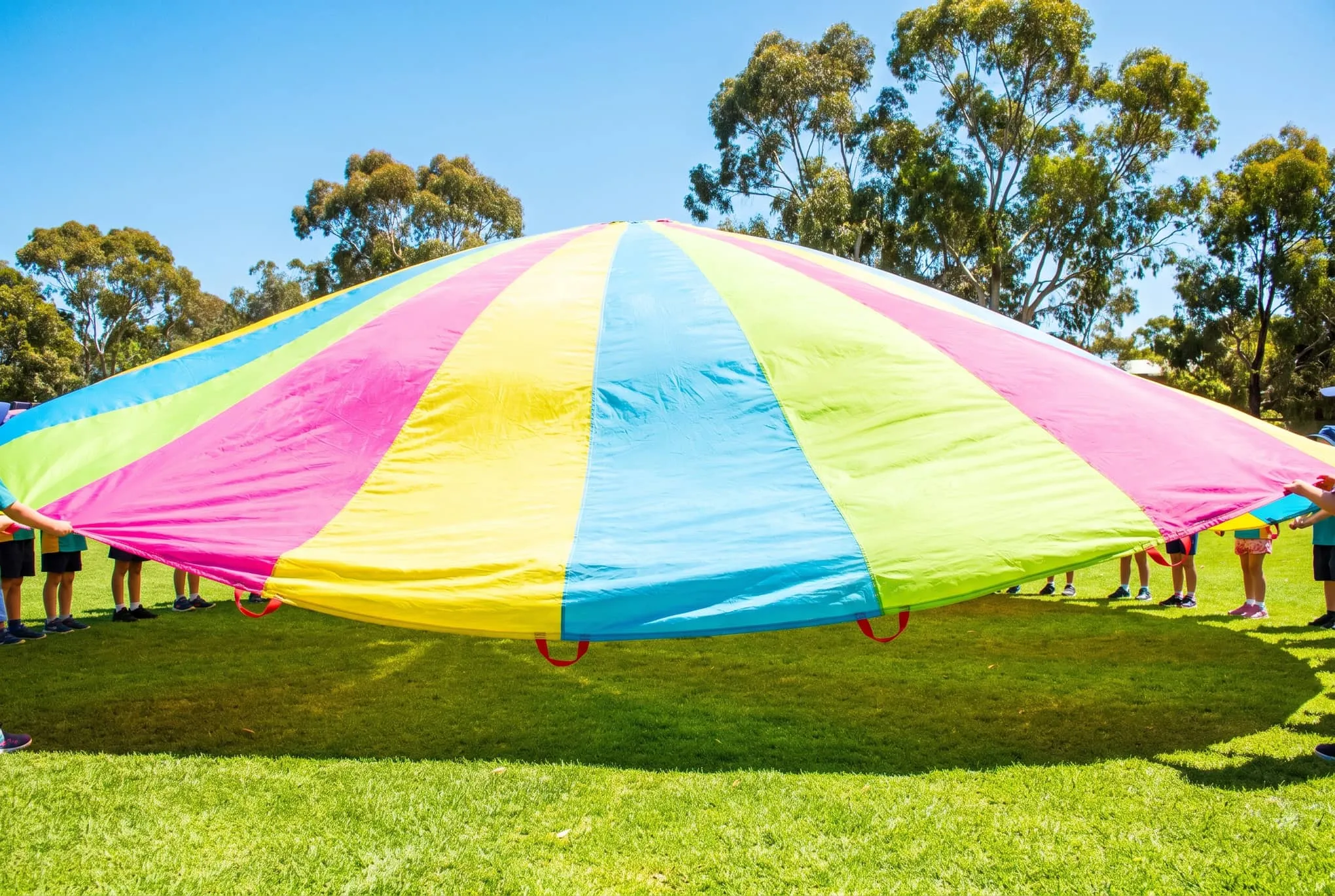 Small hands lifting a rainbow play parachute on a sunny school oval