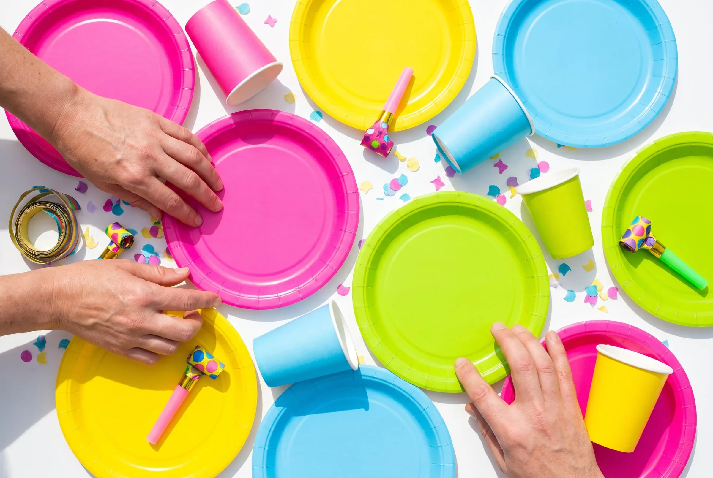 Hands setting out bright party plates and cups on a white table