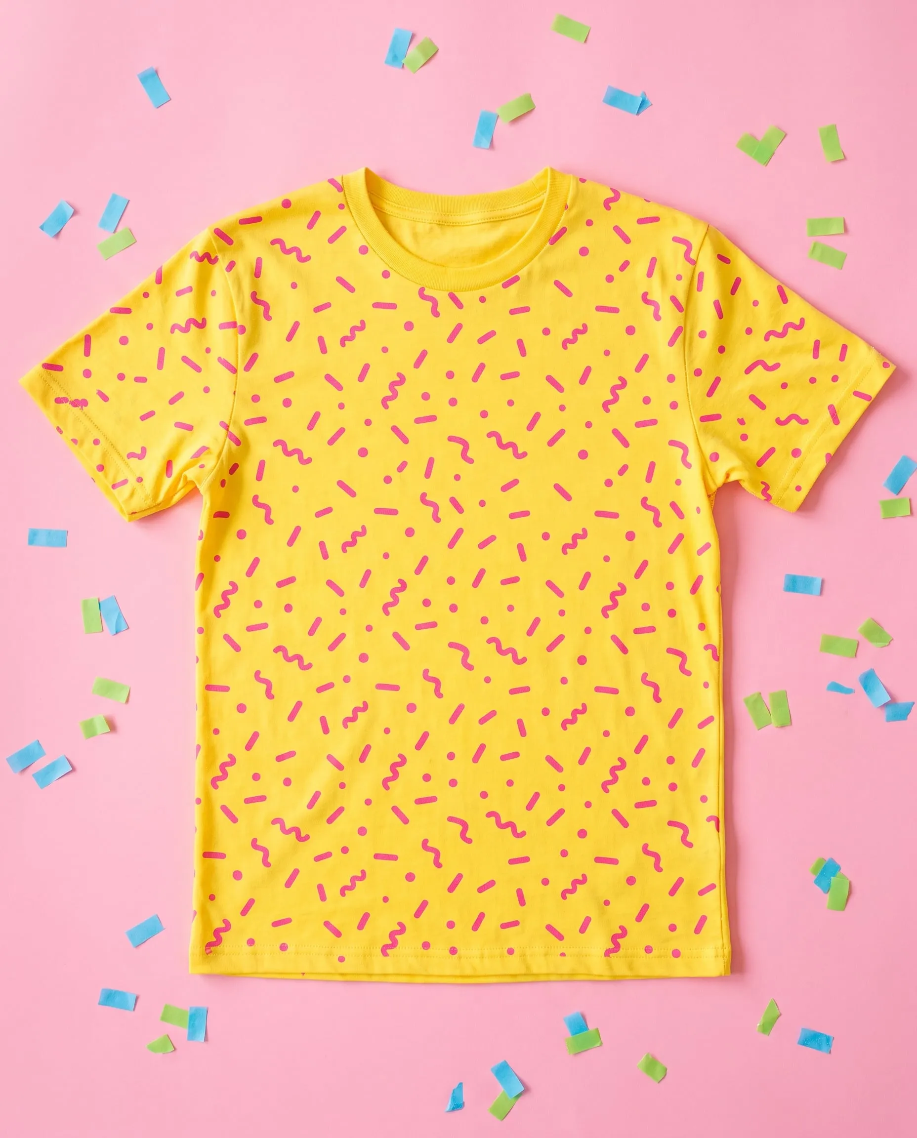 A sunshine yellow T-shirt with a pink confetti print laid flat on a pink background