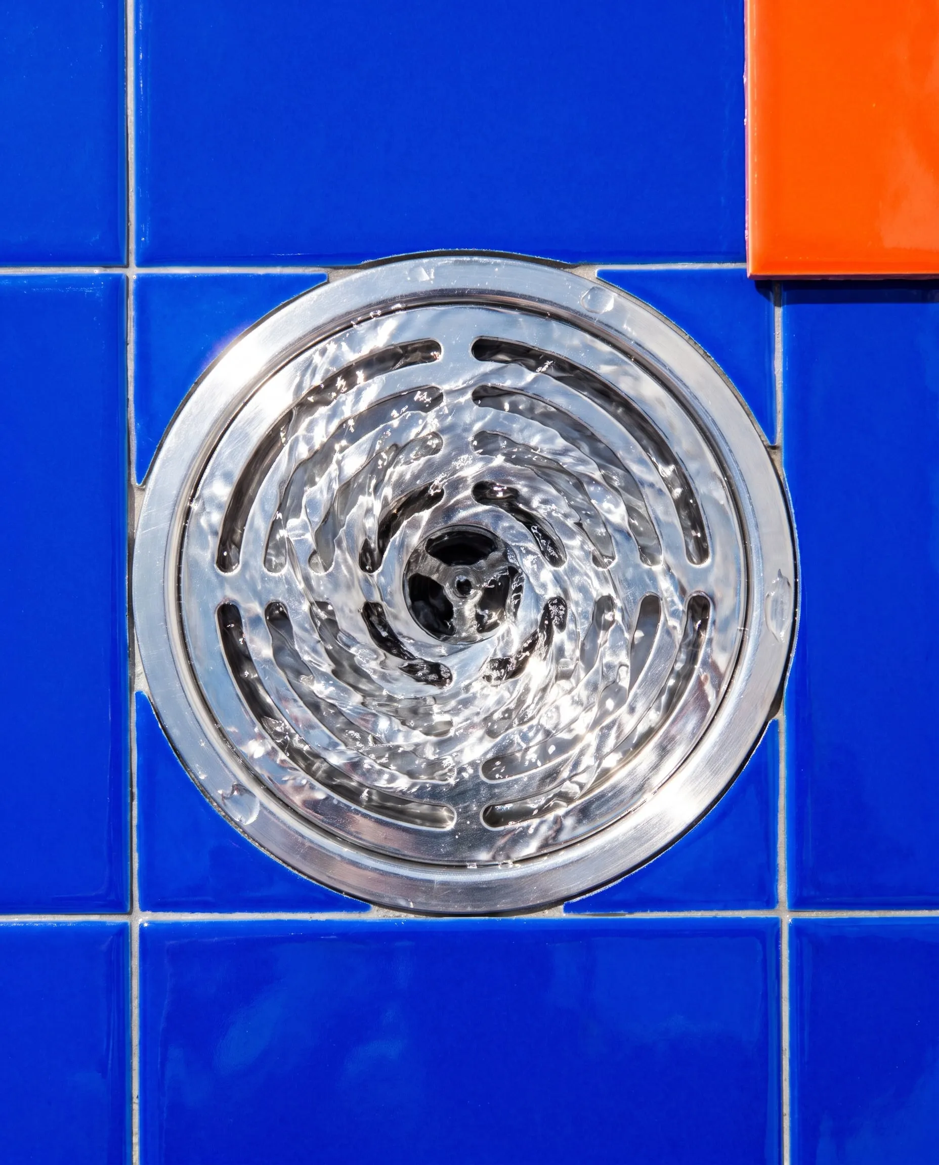 Water swirling into a round steel floor drain set in bright blue tiles