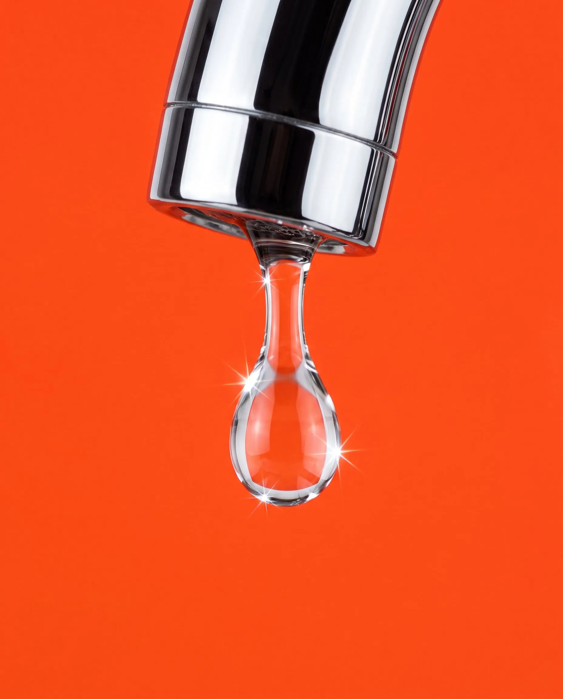 A single water droplet falling from a chrome tap against hot orange