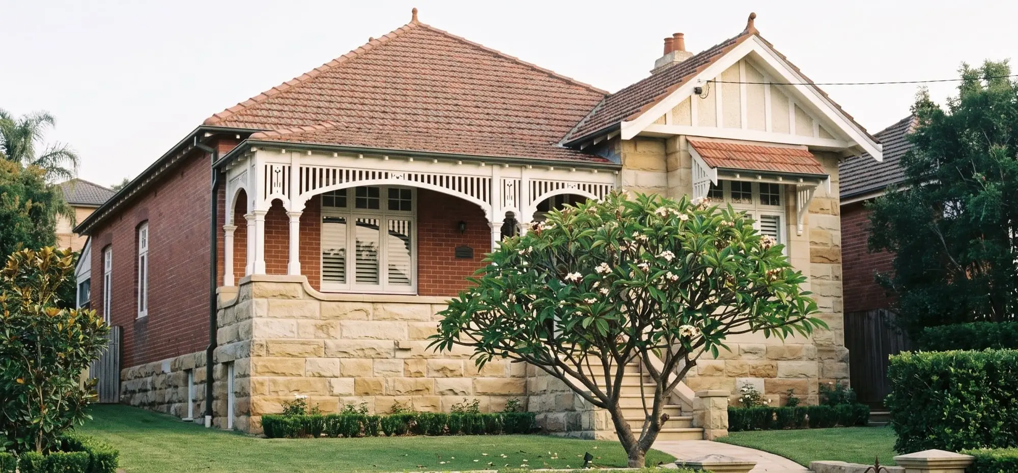 Federation house with a sandstone base, white timber verandah and a frangipani in the front garden