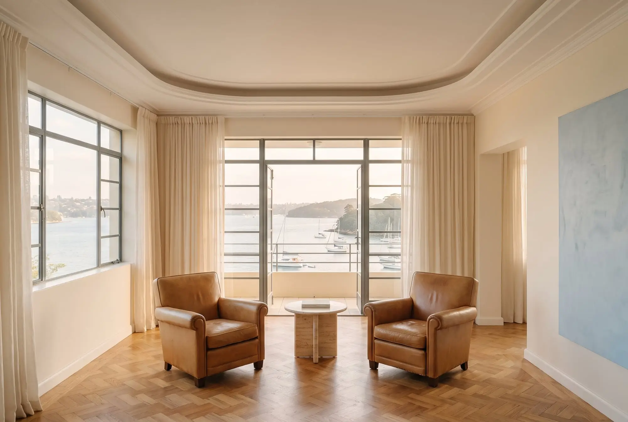Art Deco living room with two leather armchairs and steel-framed doors open to a harbour view with yachts