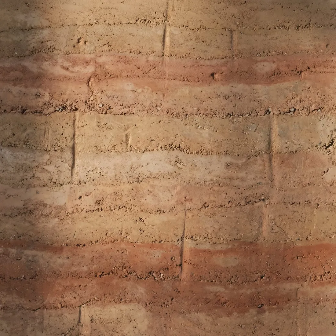 Close view of a rammed earth wall showing its compacted layers in ochre, clay and rust tones