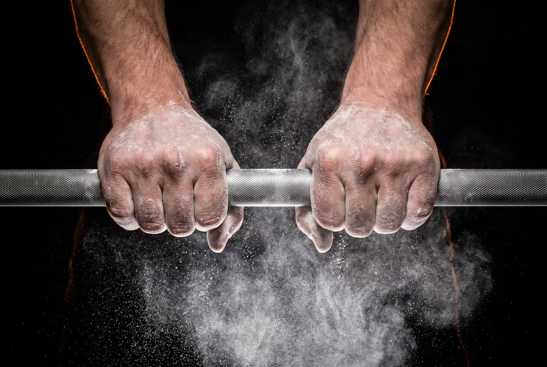 Chalked hands gripping a knurled barbell in a cloud of white chalk