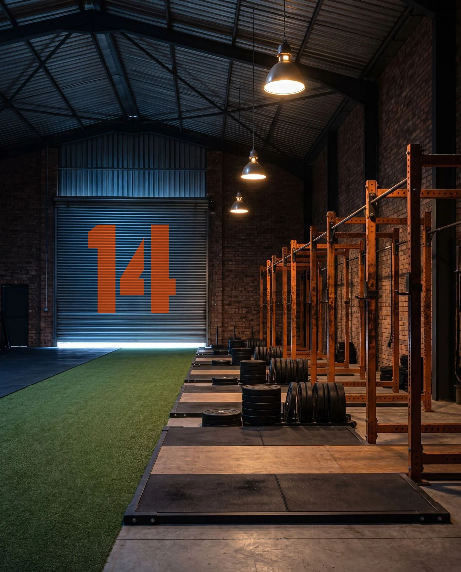 Inside the warehouse before sunrise: a giant orange 14 painted on the closed roller door, turf and racks running toward it