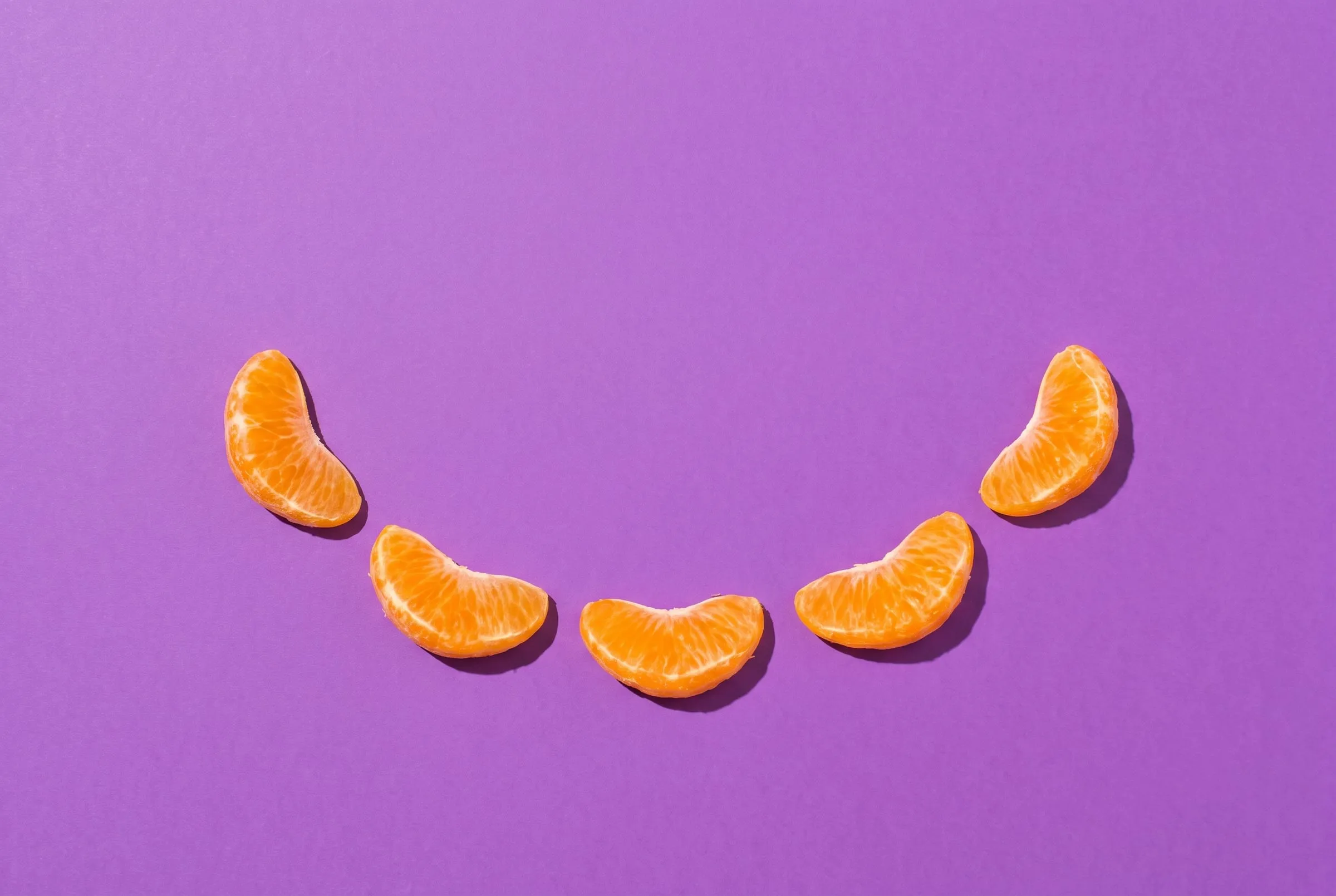 Mandarin segments arranged in a smile on grape purple paper