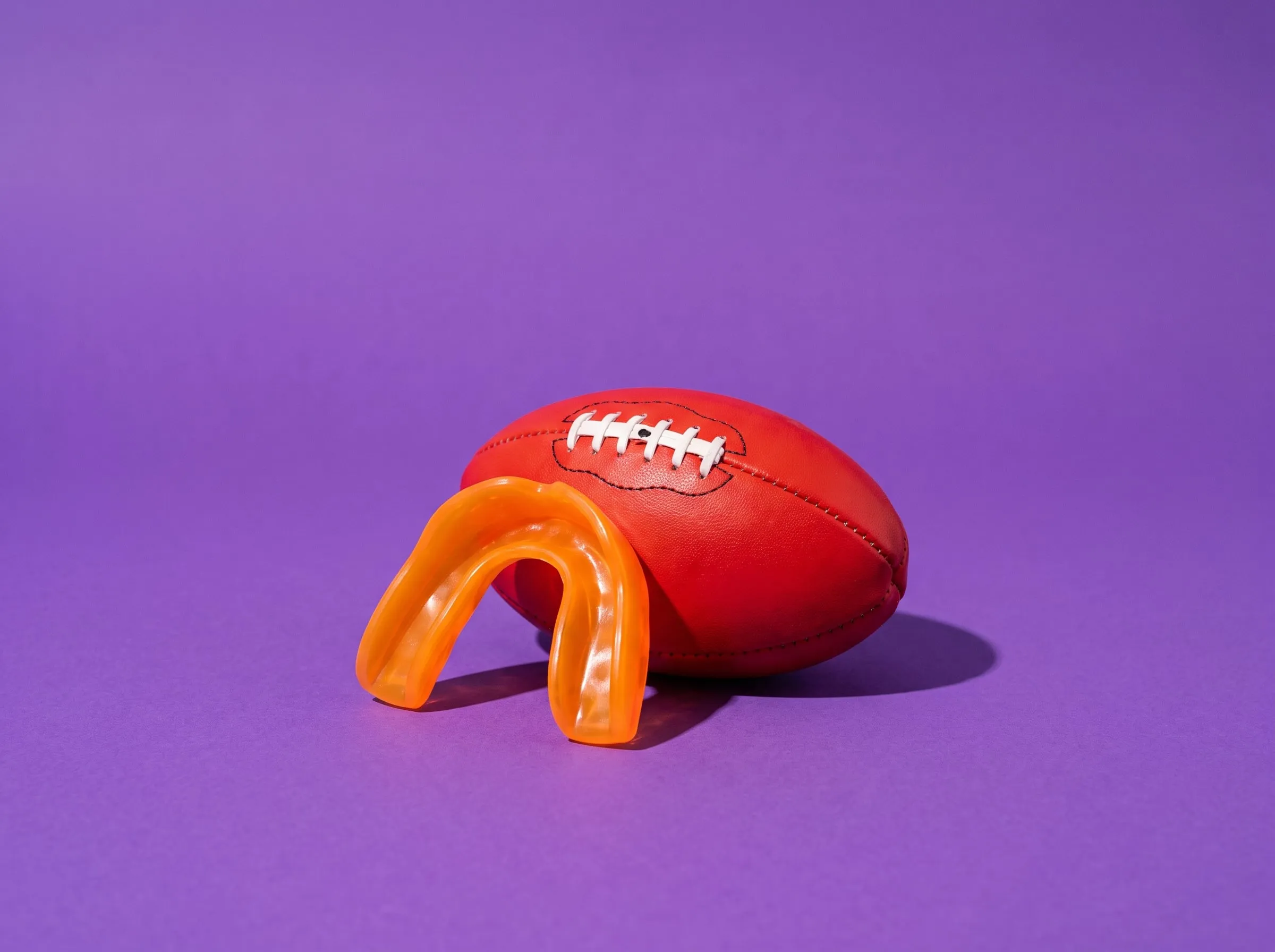 An orange sports mouthguard in front of a red Australian rules football