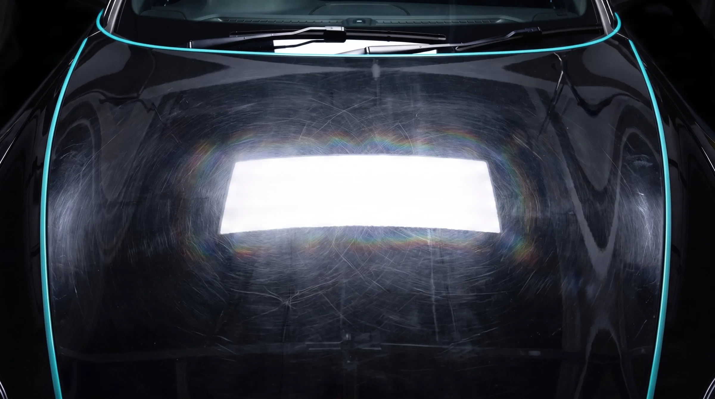 Black bonnet under an LED inspection light showing circular swirl marks and holograms