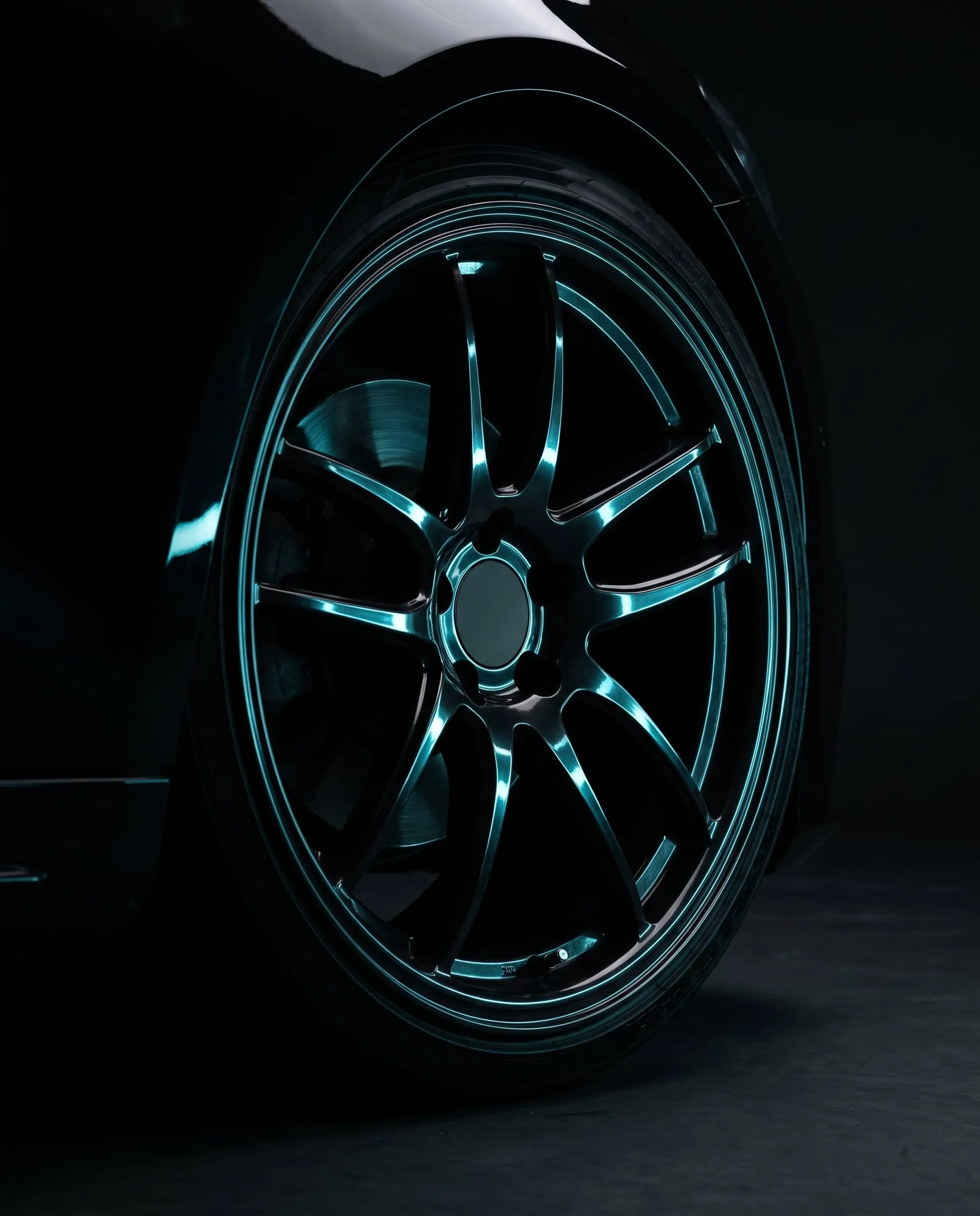 Black alloy wheel catching cyan light in a dark studio