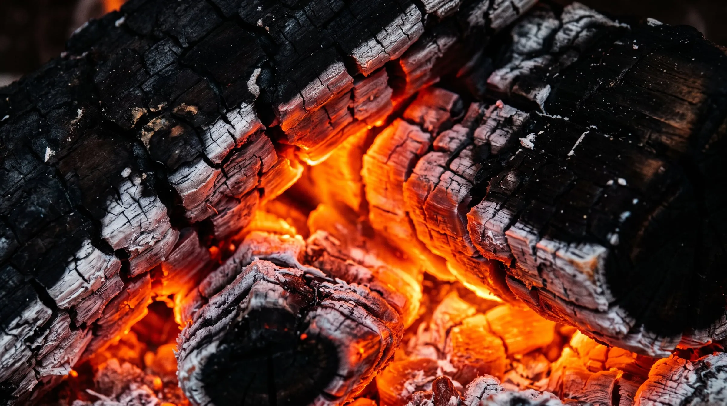 Glowing orange embers and charred hardwood inside a wood-fired oven