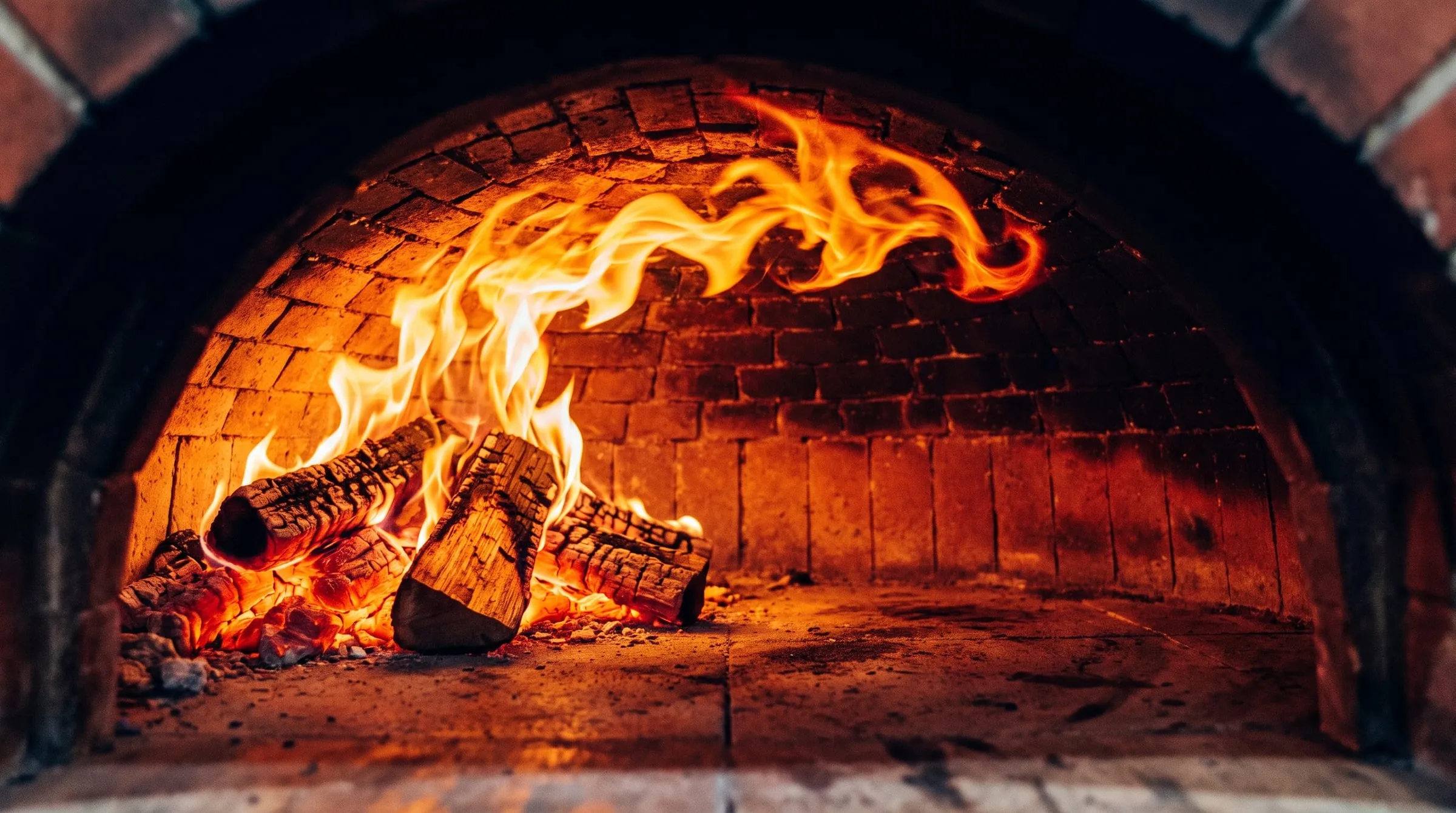 Flames curling across the brick dome of a wood-fired oven at full heat