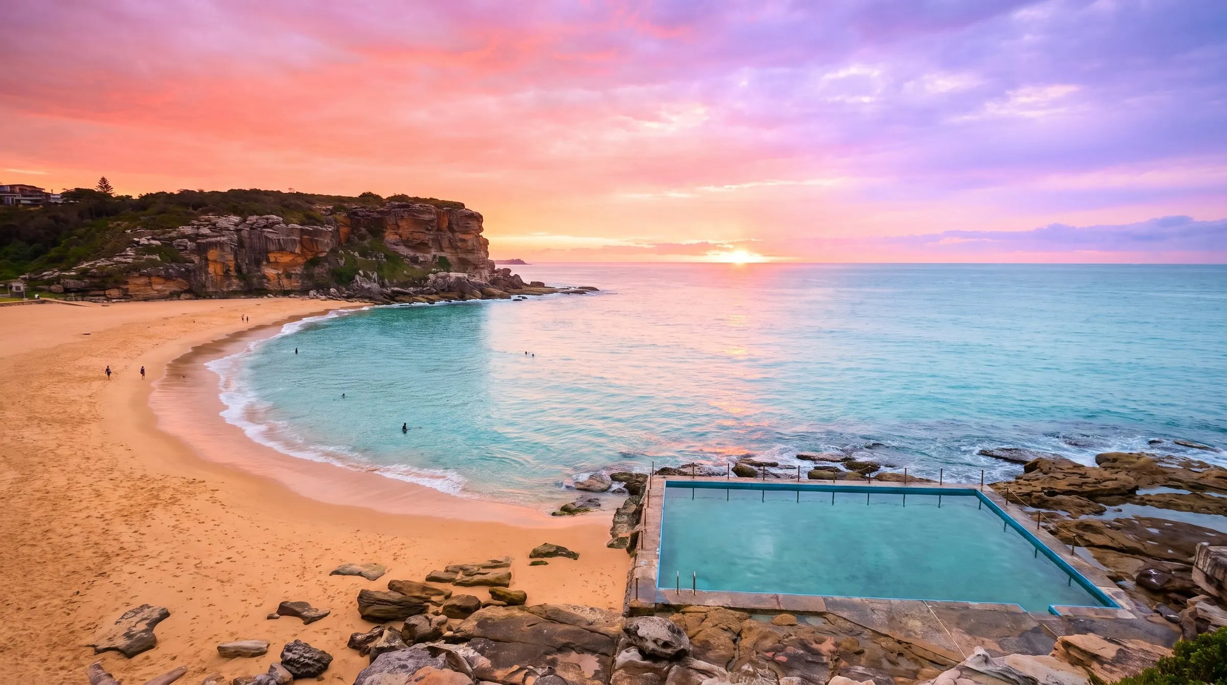 A Sydney ocean beach and rock pool at sunrise, the sky glowing coral and violet