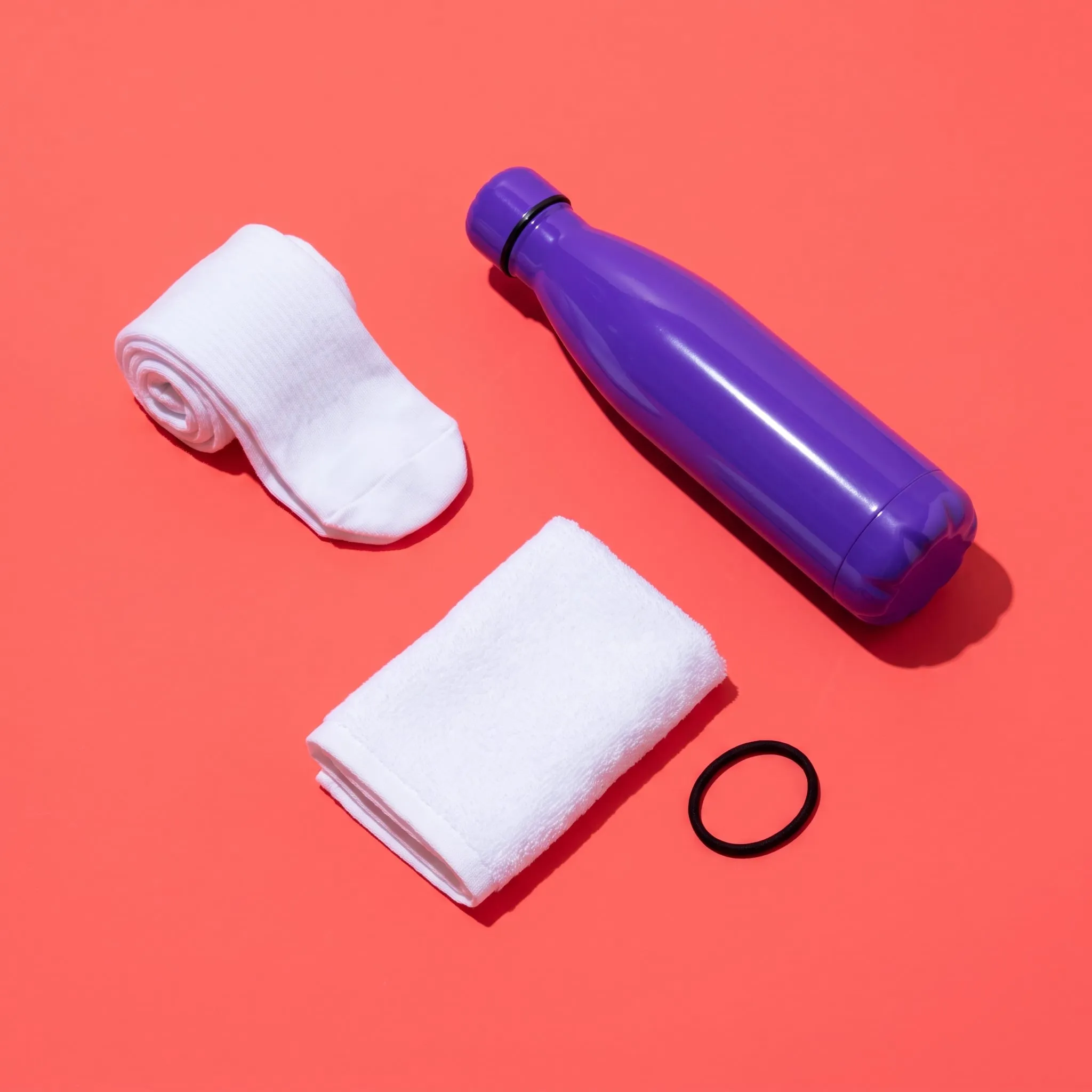 Grip socks, a violet water bottle, a towel and a hair tie on coral