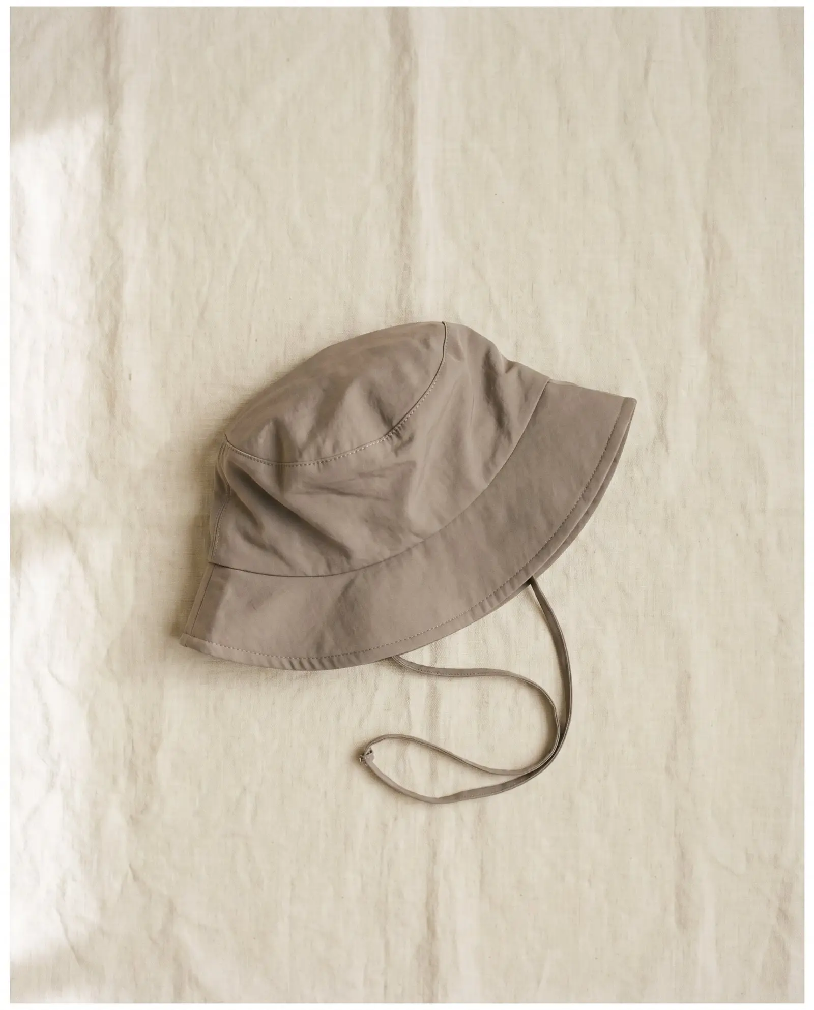 Salt bucket hat in Driftwood, laid flat on sand-coloured linen