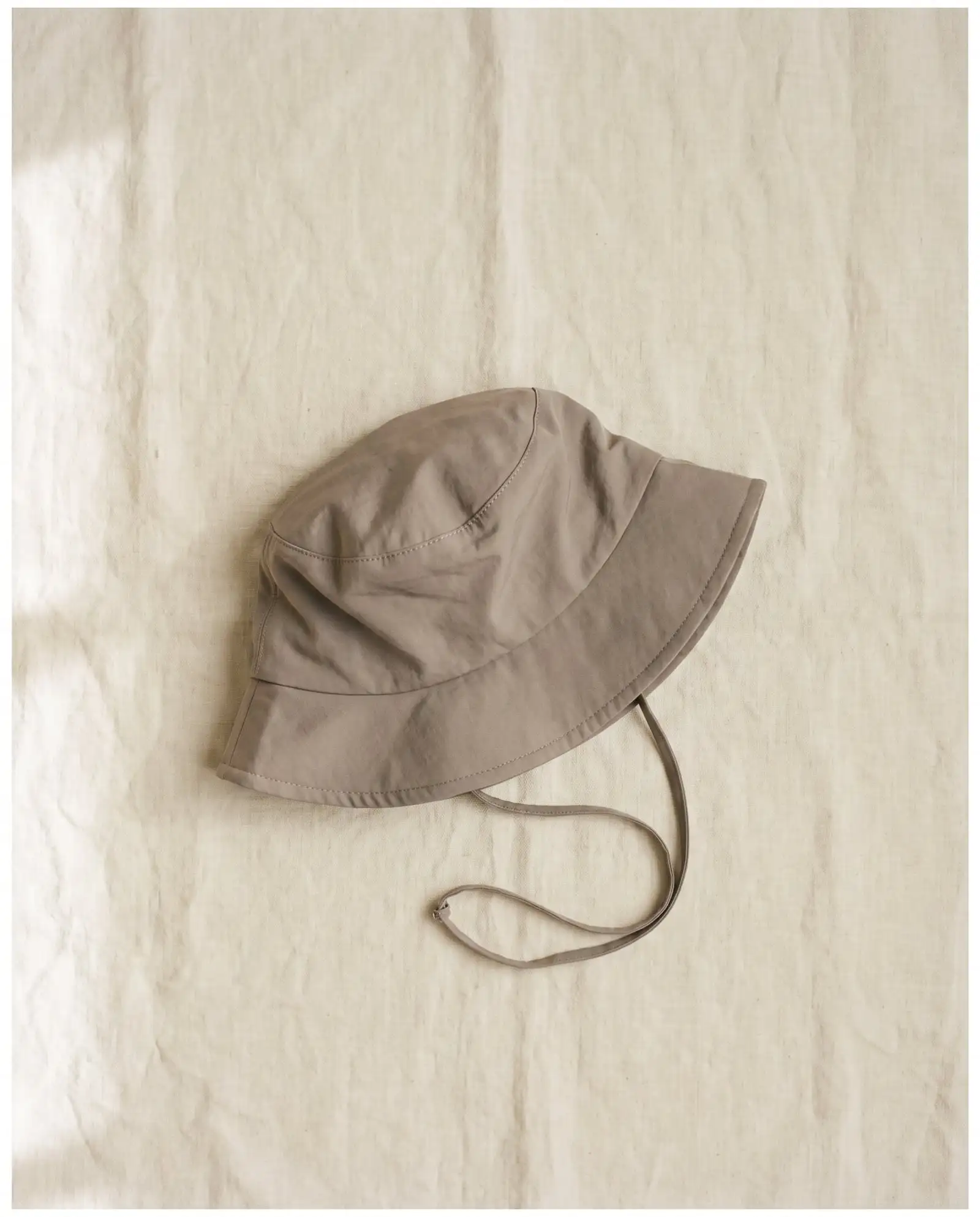 Salt bucket hat in Driftwood, laid flat on sand-coloured linen