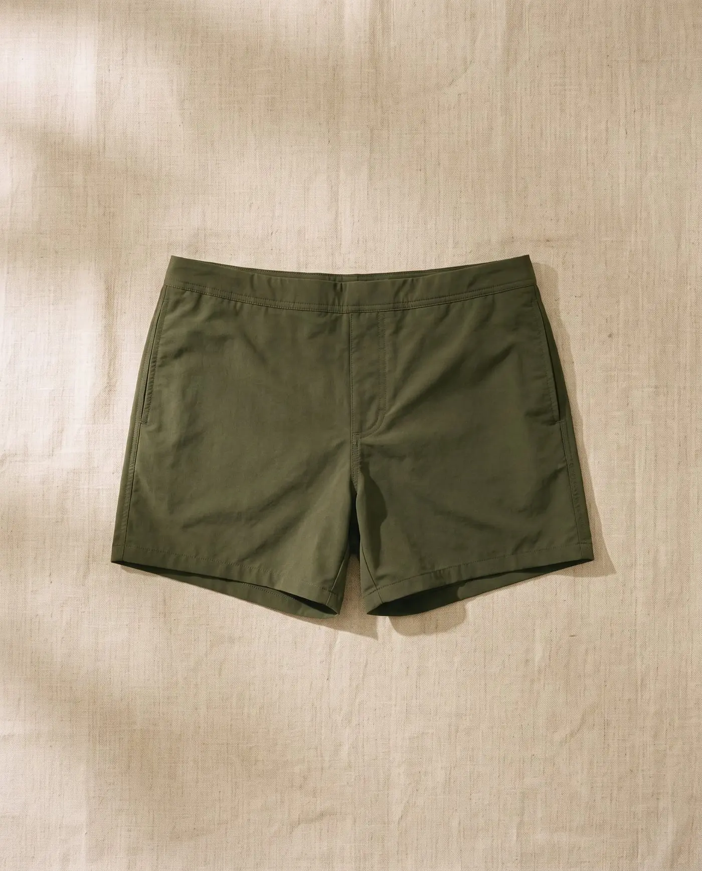 Lennox swim trunk in Kelp, laid flat on sand-coloured linen