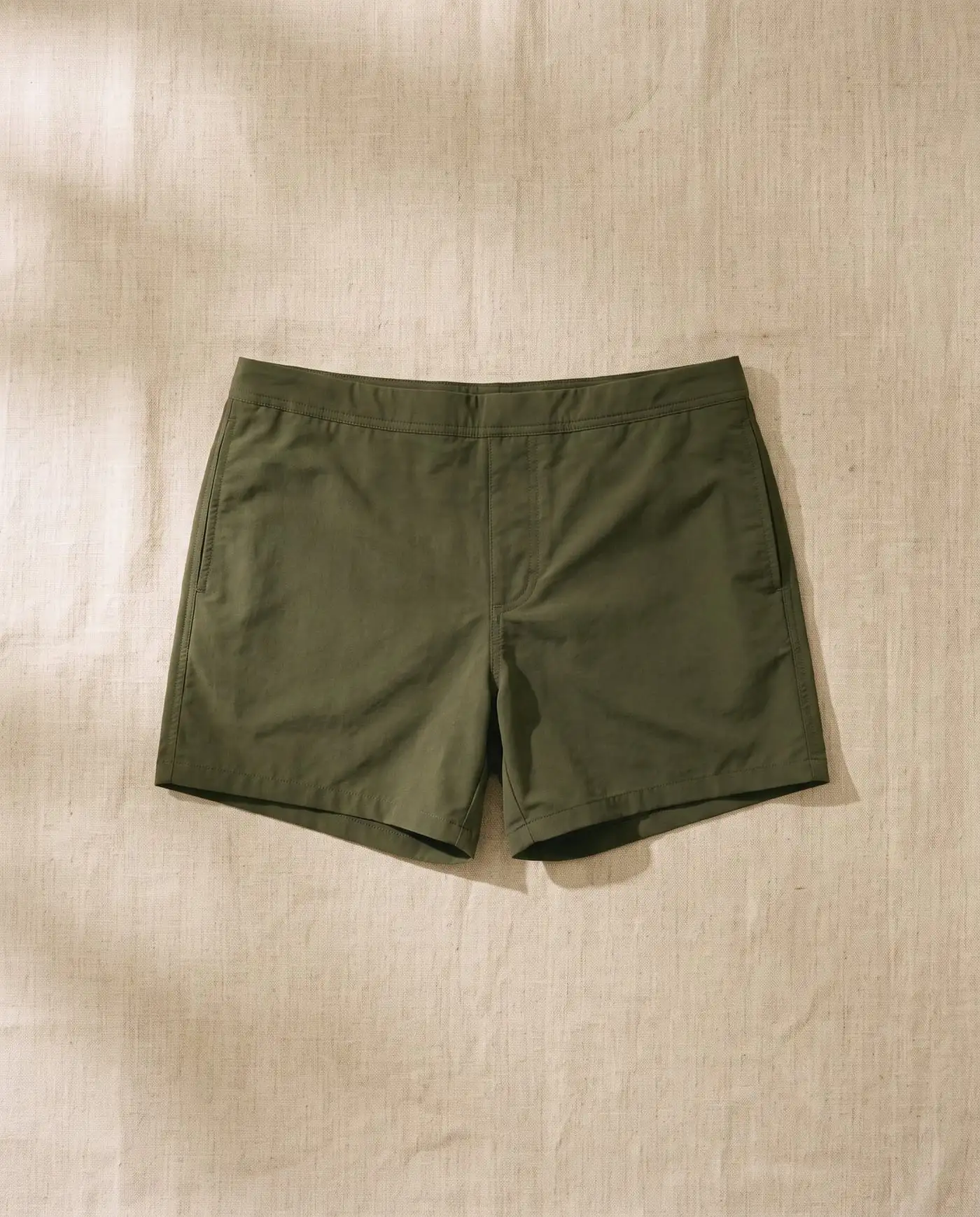 Lennox swim trunk in Kelp, laid flat on sand-coloured linen
