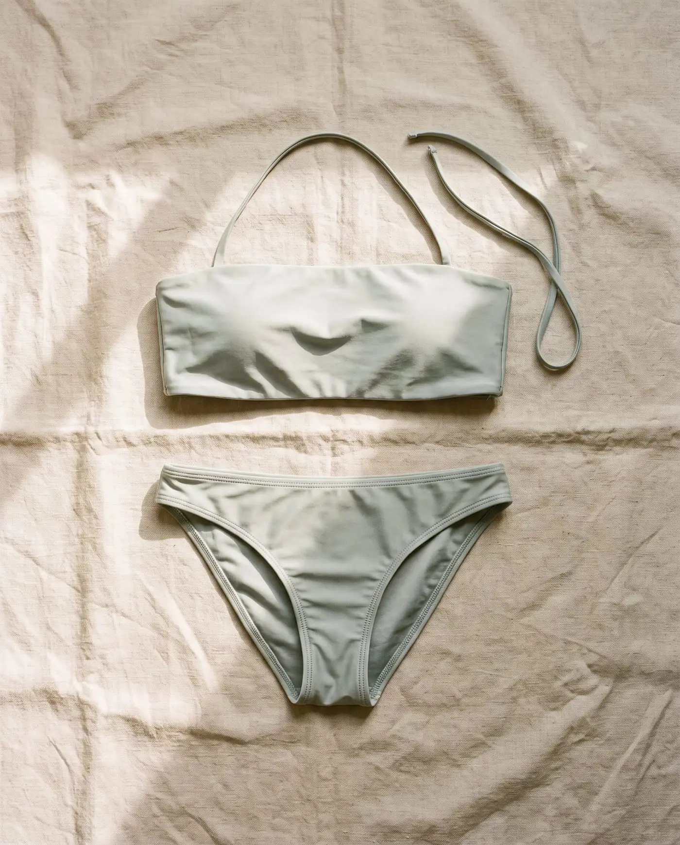 Low Tide bandeau bikini set in Saltbush, laid flat on sand-coloured linen