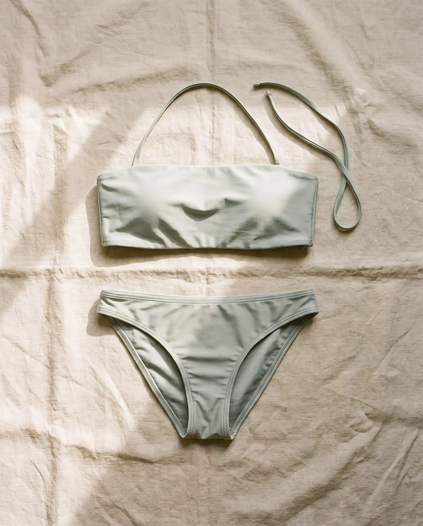 Low Tide bandeau bikini set in Saltbush, laid flat on sand-coloured linen