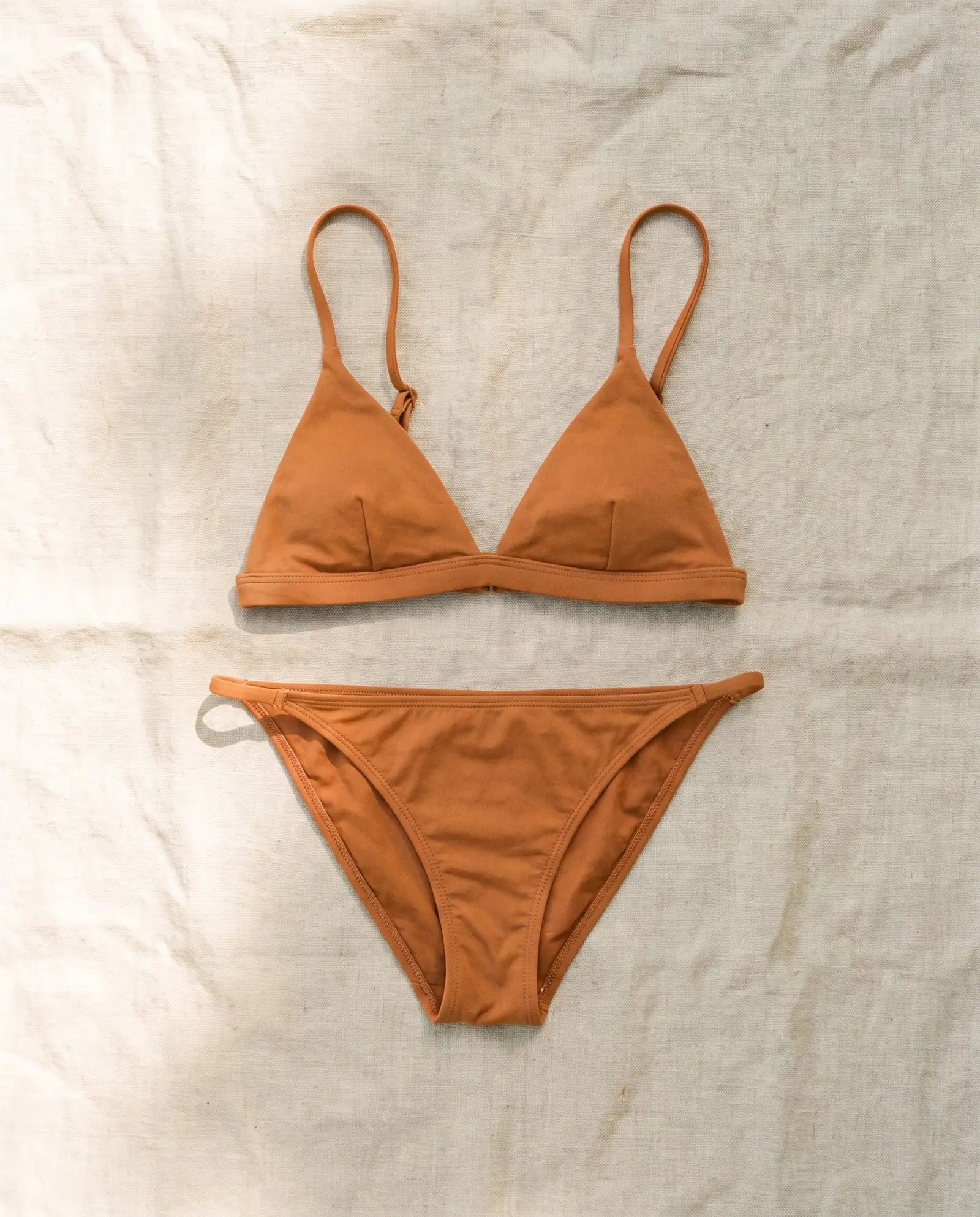 Shell triangle bikini set in Ochre, laid flat on sand-coloured linen