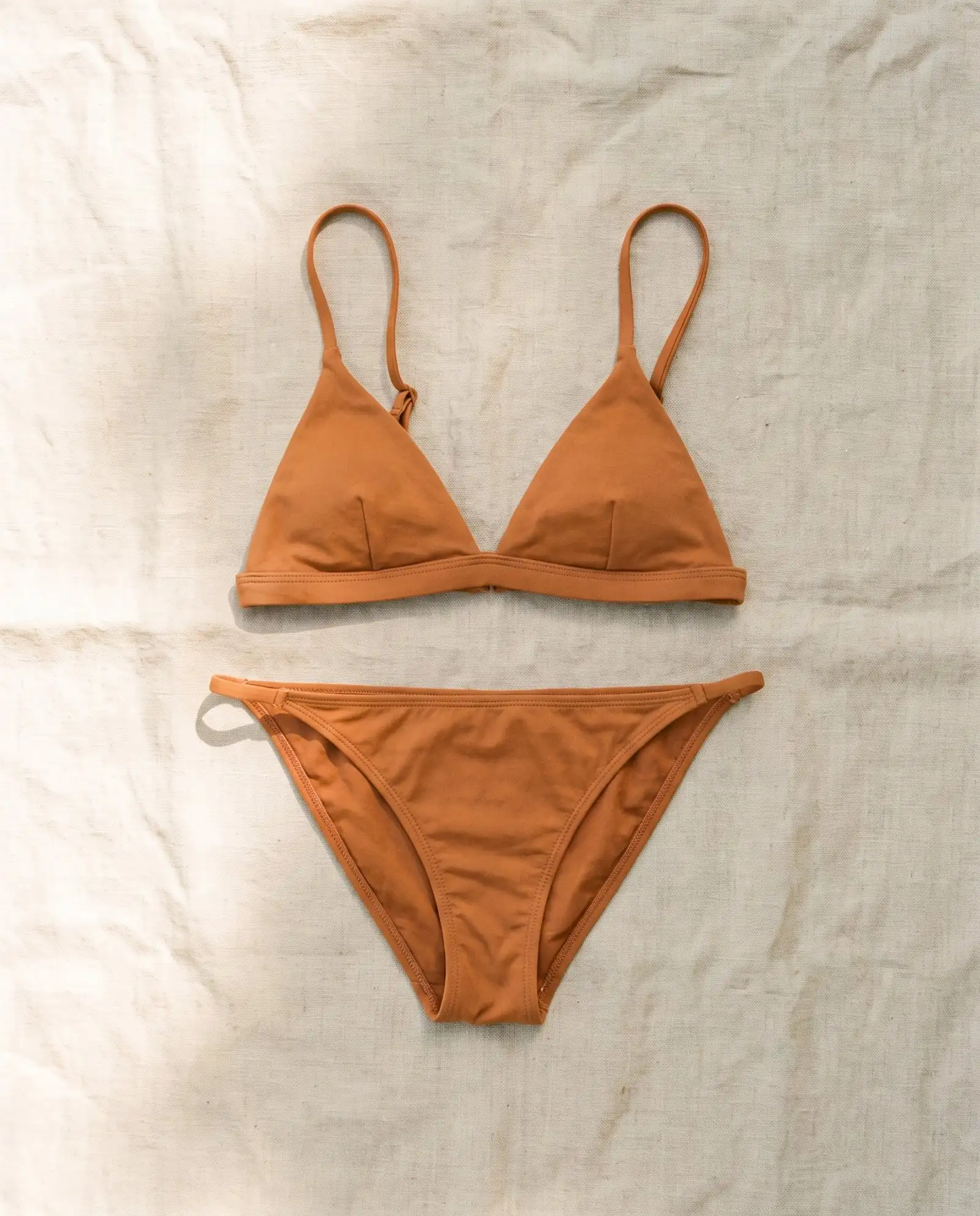 Shell triangle bikini set in Ochre, laid flat on sand-coloured linen