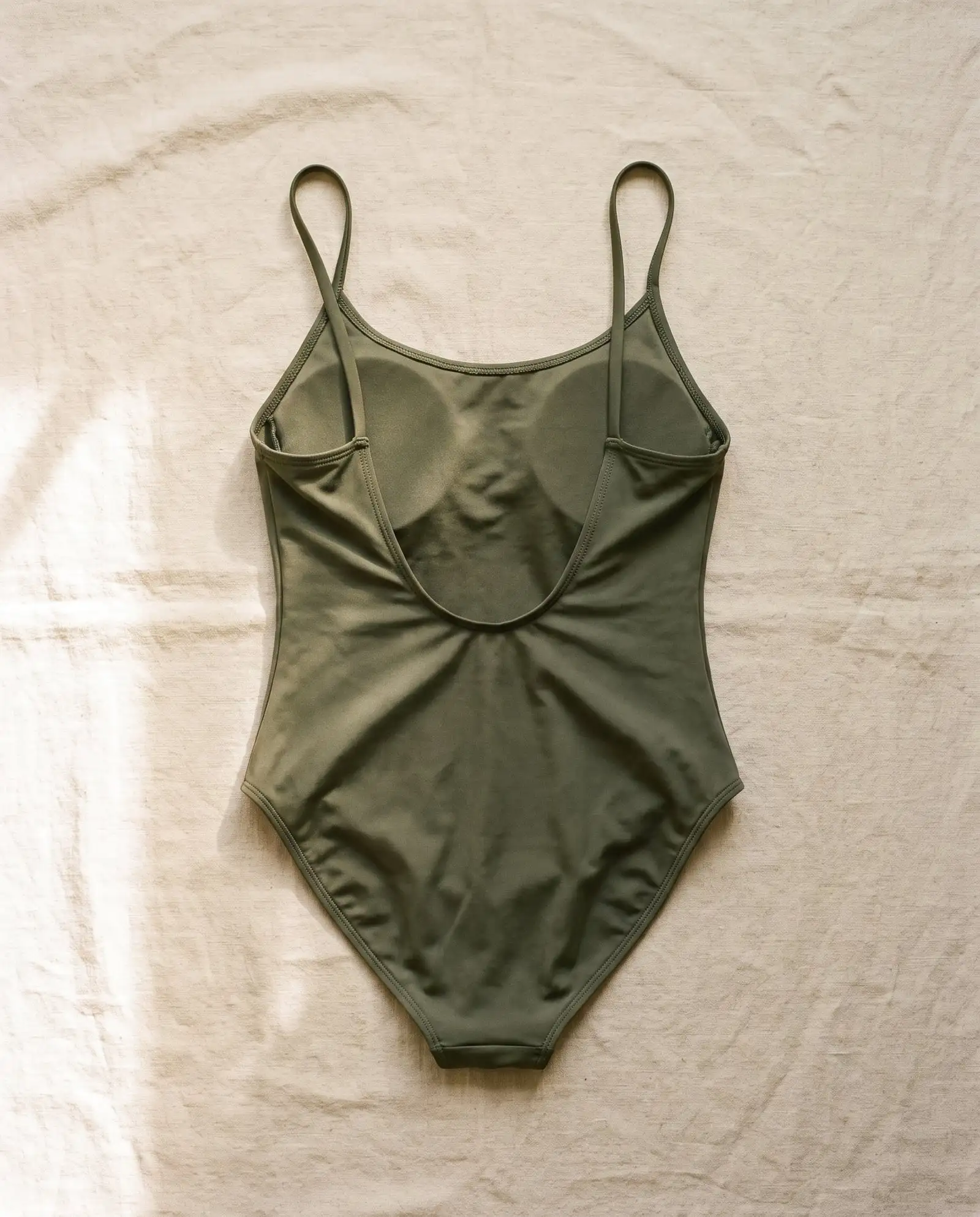 Tallow scoop back one-piece in Kelp, laid flat on sand-coloured linen