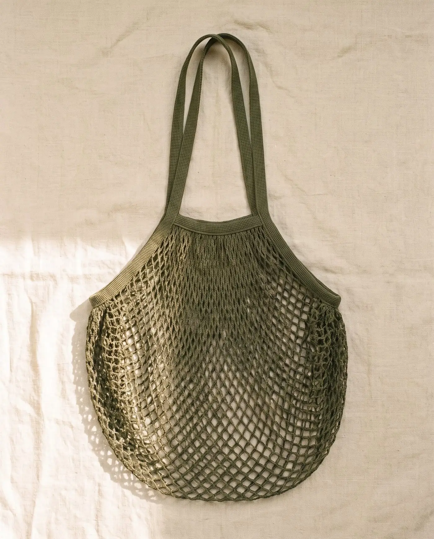 Rinse mesh tote in Kelp, laid flat on sand-coloured linen