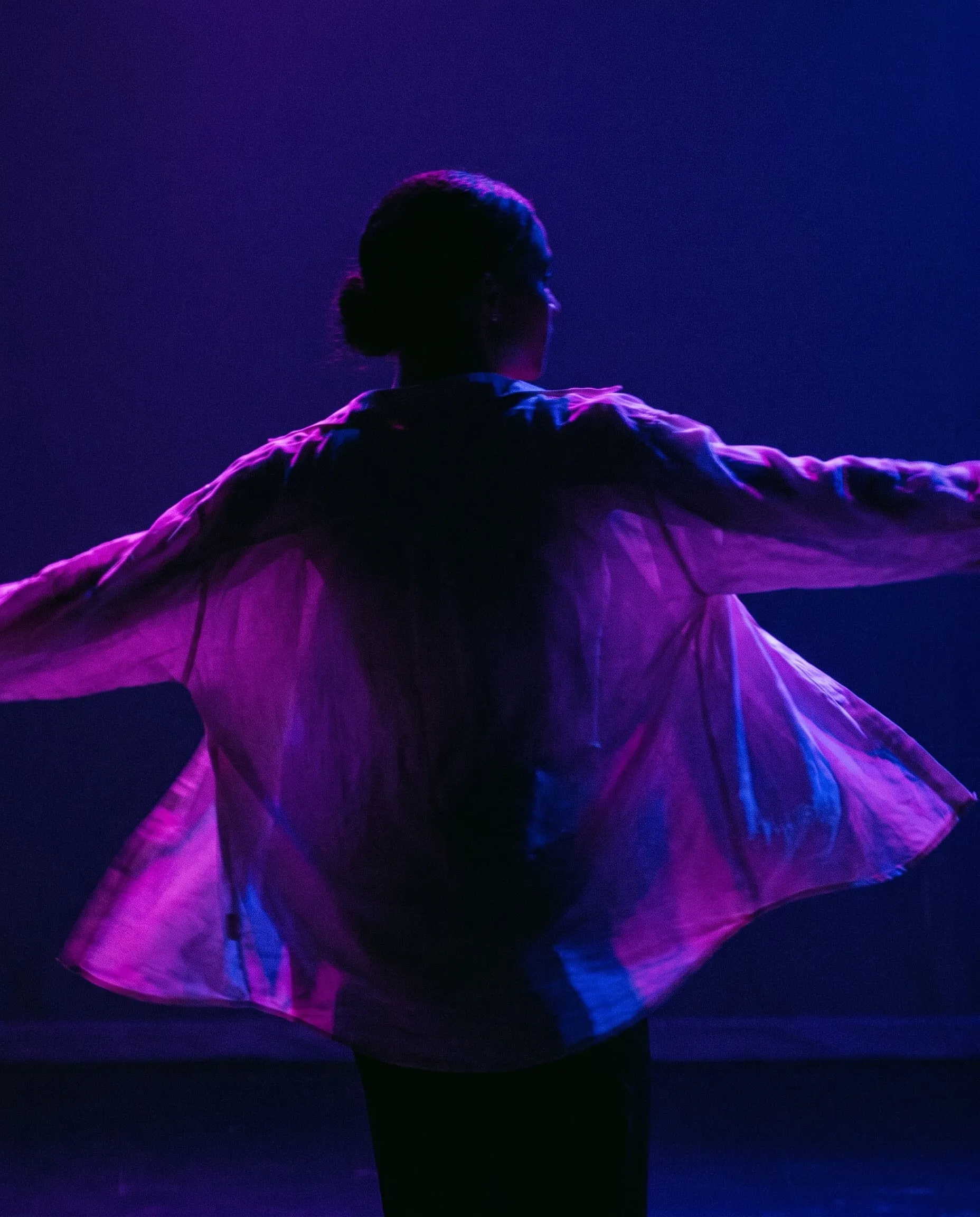 A dancer mid-turn, a loose shirt sweeping out in violet and magenta light