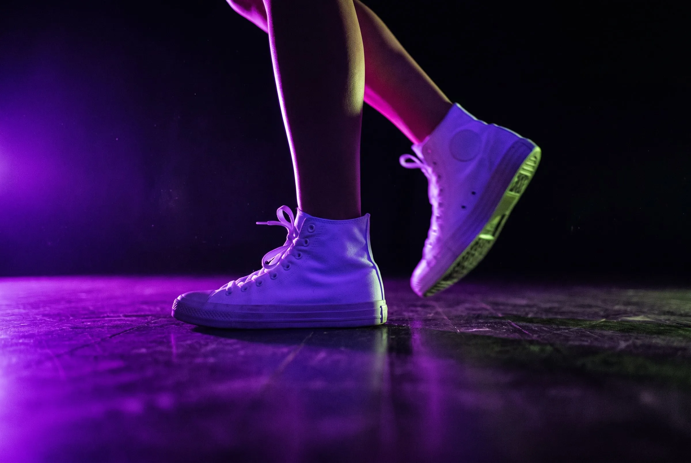 White high-top sneakers mid-step on a dark timber floor in violet light
