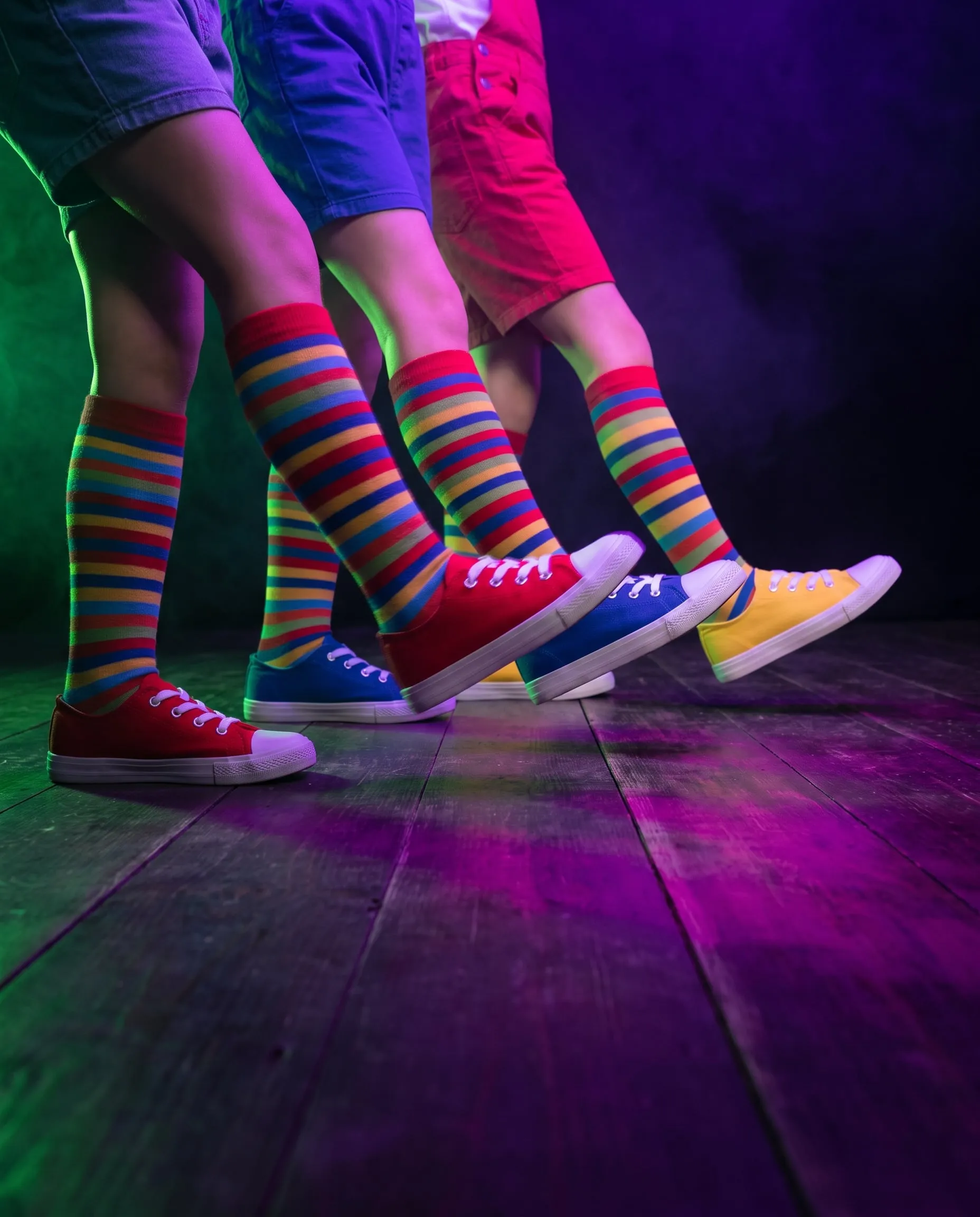 Three children in bright sneakers and striped socks stepping out together on a dark dance floor
