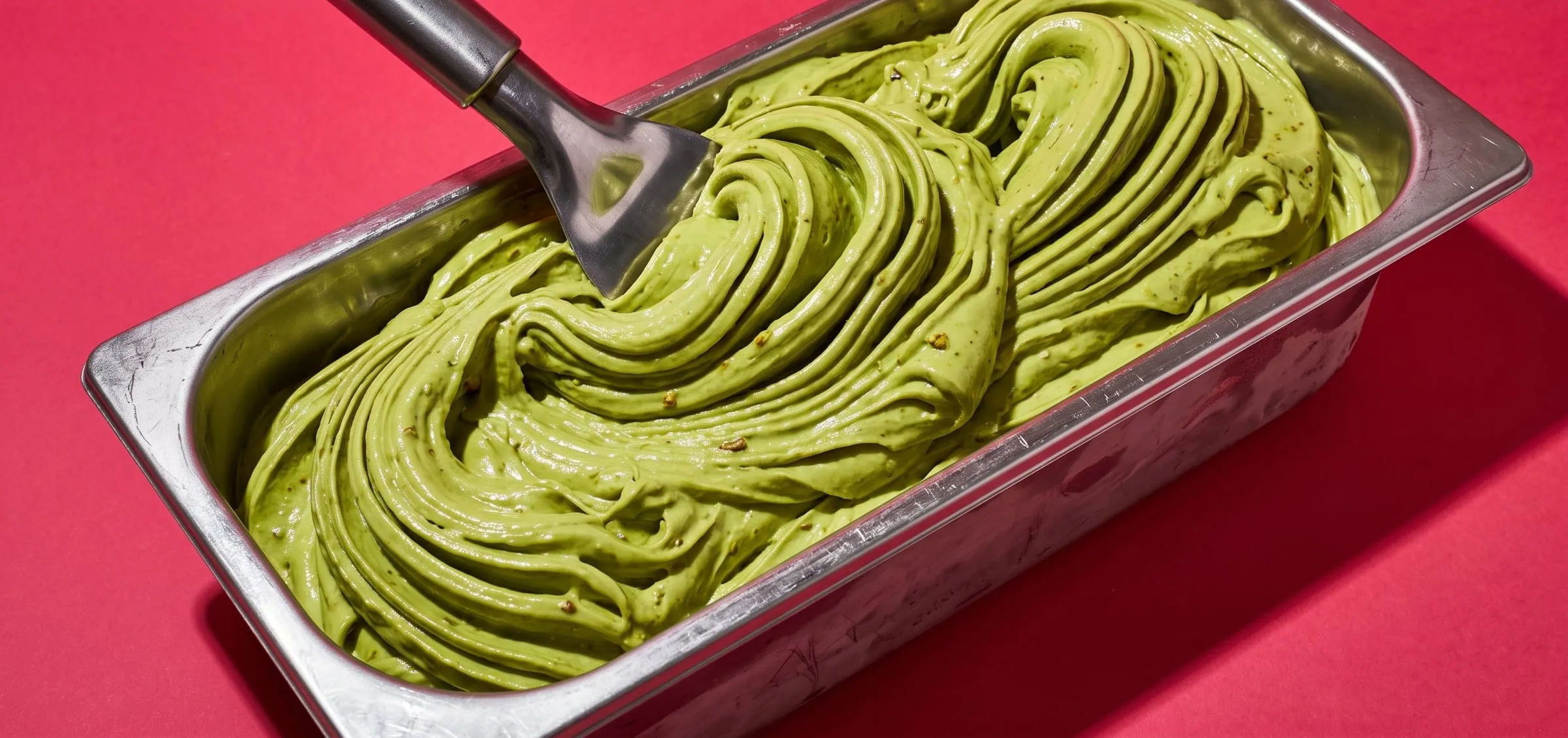Freshly churned pistachio gelato swept into deep glossy waves in a steel tray on raspberry pink paper
