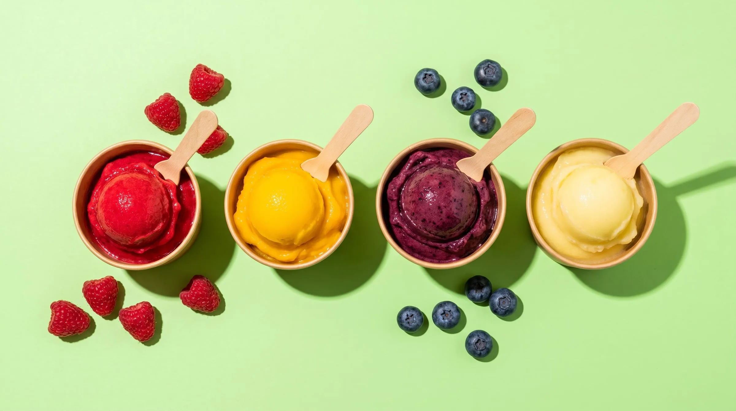 Four cups of fruit sorbet in raspberry, mango, blueberry and lemon on a pistachio green backdrop