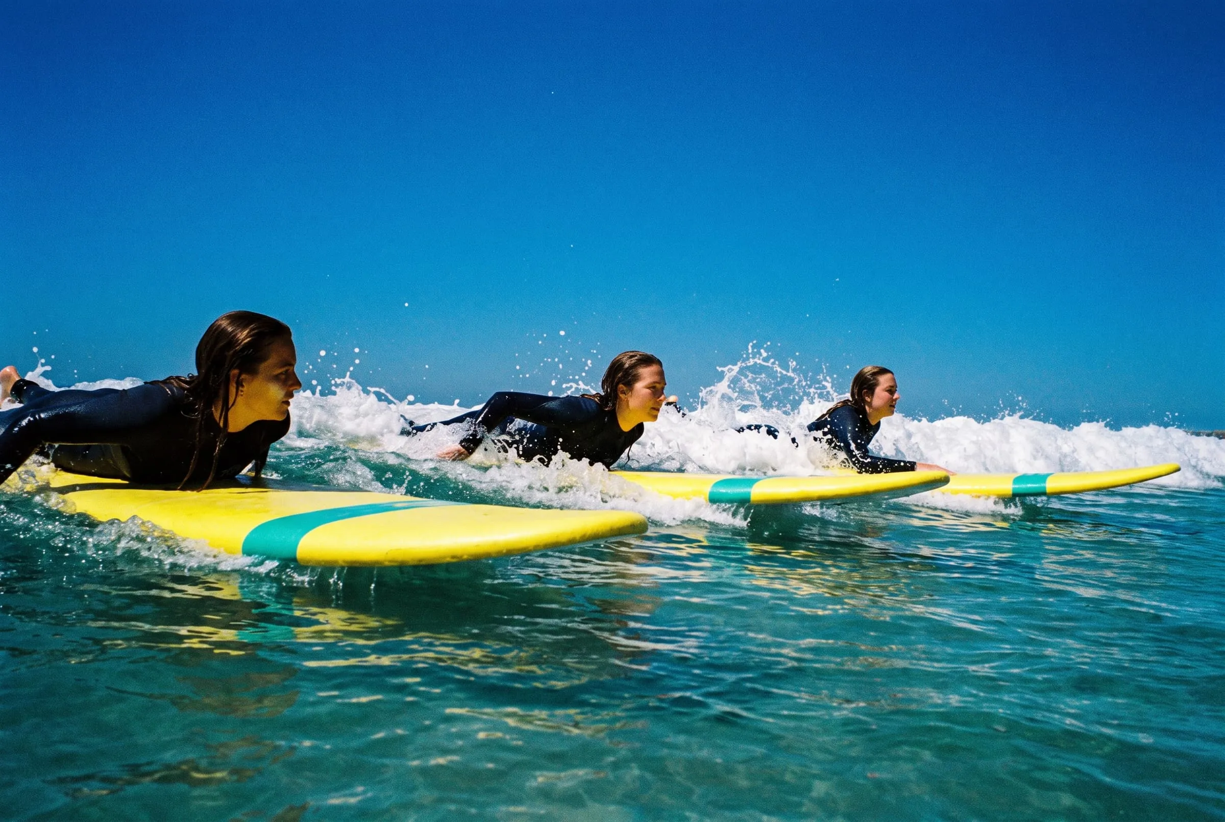 Three women on yellow soft-tops paddle out together through a line of small whitewater.