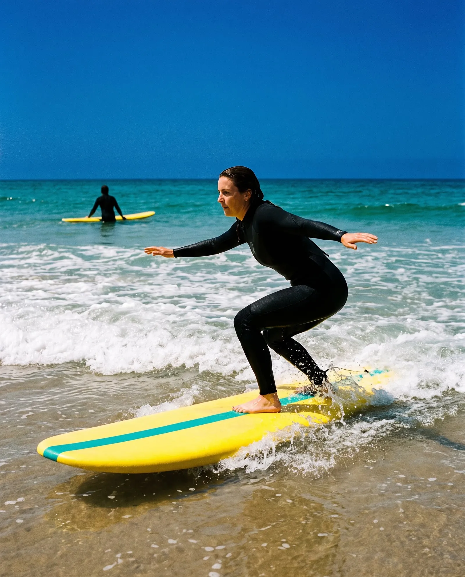 A woman rises to her feet on a yellow soft-top in small whitewater, arms out for balance.