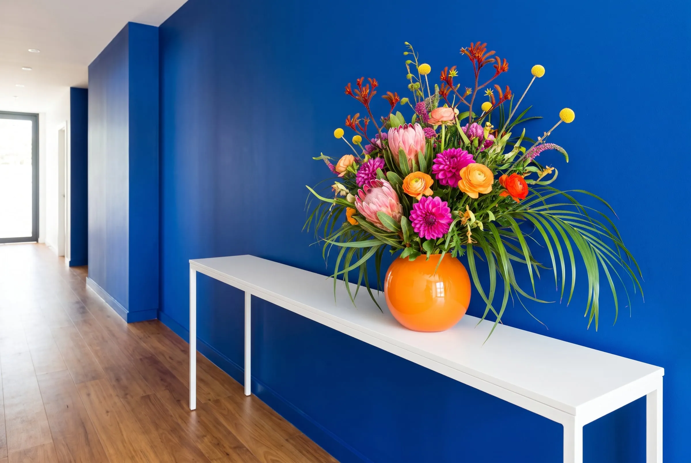 A big loose arrangement in an orange vase on a white console table against a cobalt hotel corridor wall
