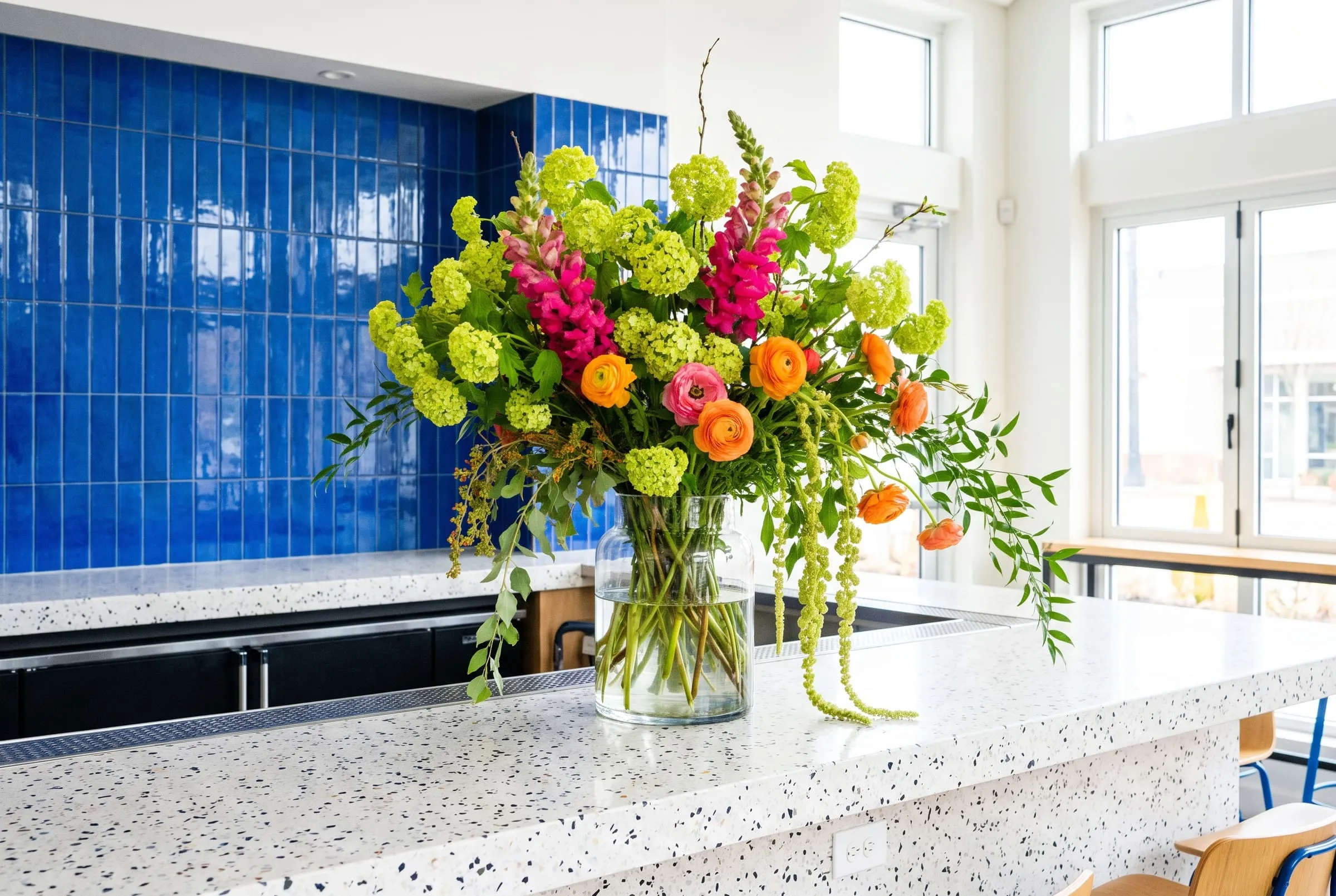 A big loose arrangement of lime green and hot pink flowers on a terrazzo bar in front of cobalt tiles