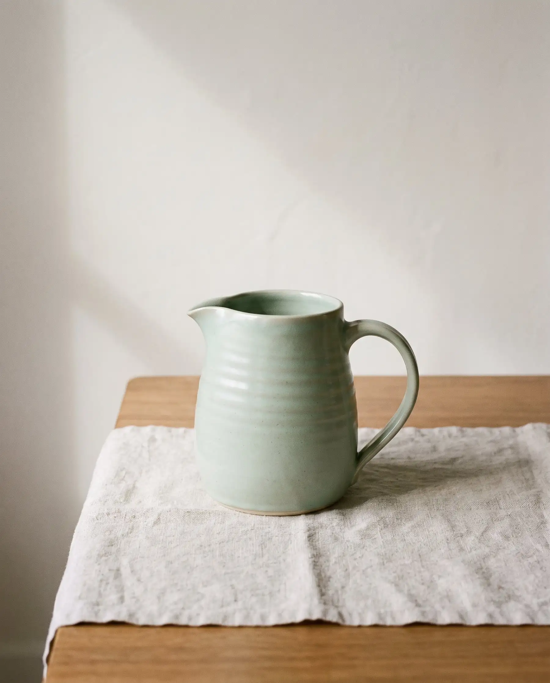 A pale celadon green pouring jug on oatmeal linen
