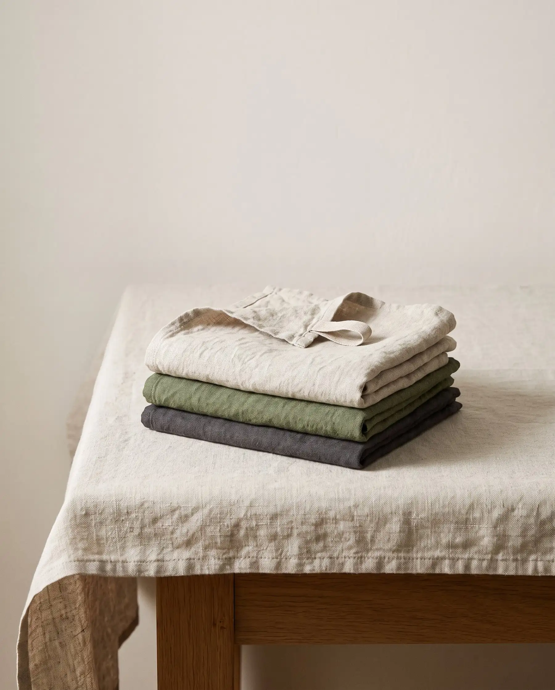 Three folded linen tea towels in oat, moss and charcoal