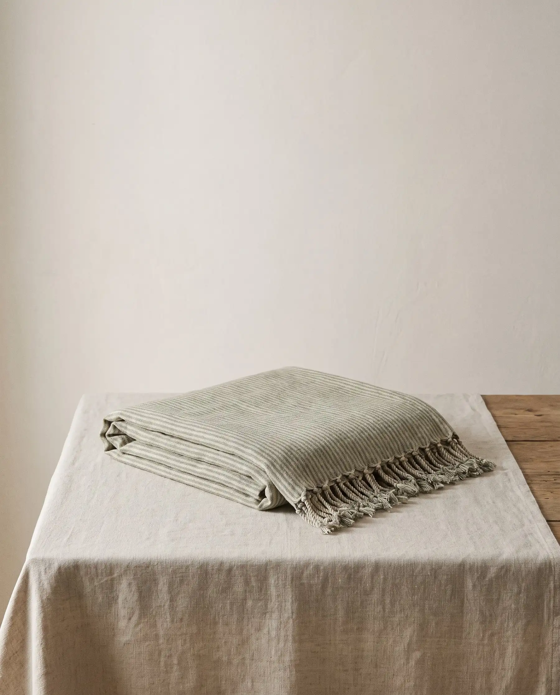 A folded sage and oatmeal striped linen throw with knotted fringe