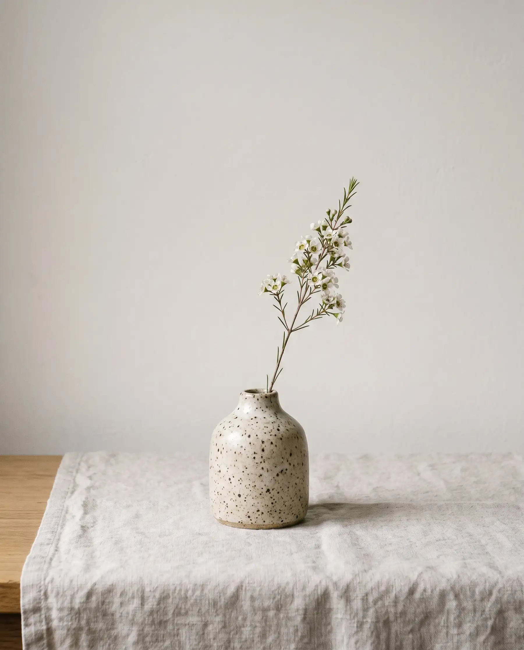 A speckled oatmeal bud vase holding a stem of white tea-tree